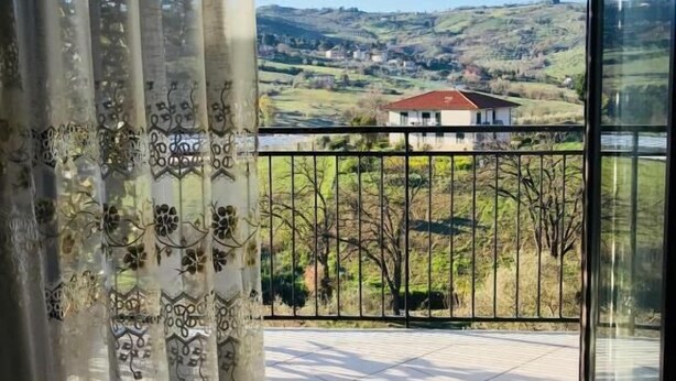 A balcony with a view of a rural landscape, including a house and rolling hills.