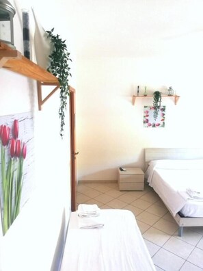 A hotel room with a bed, a bedside table with a folded towel, a nightstand, a wall-mounted shelf with decorative items, and a door leading to another room. - B&B Relax Damiani (Laureana Cilento)