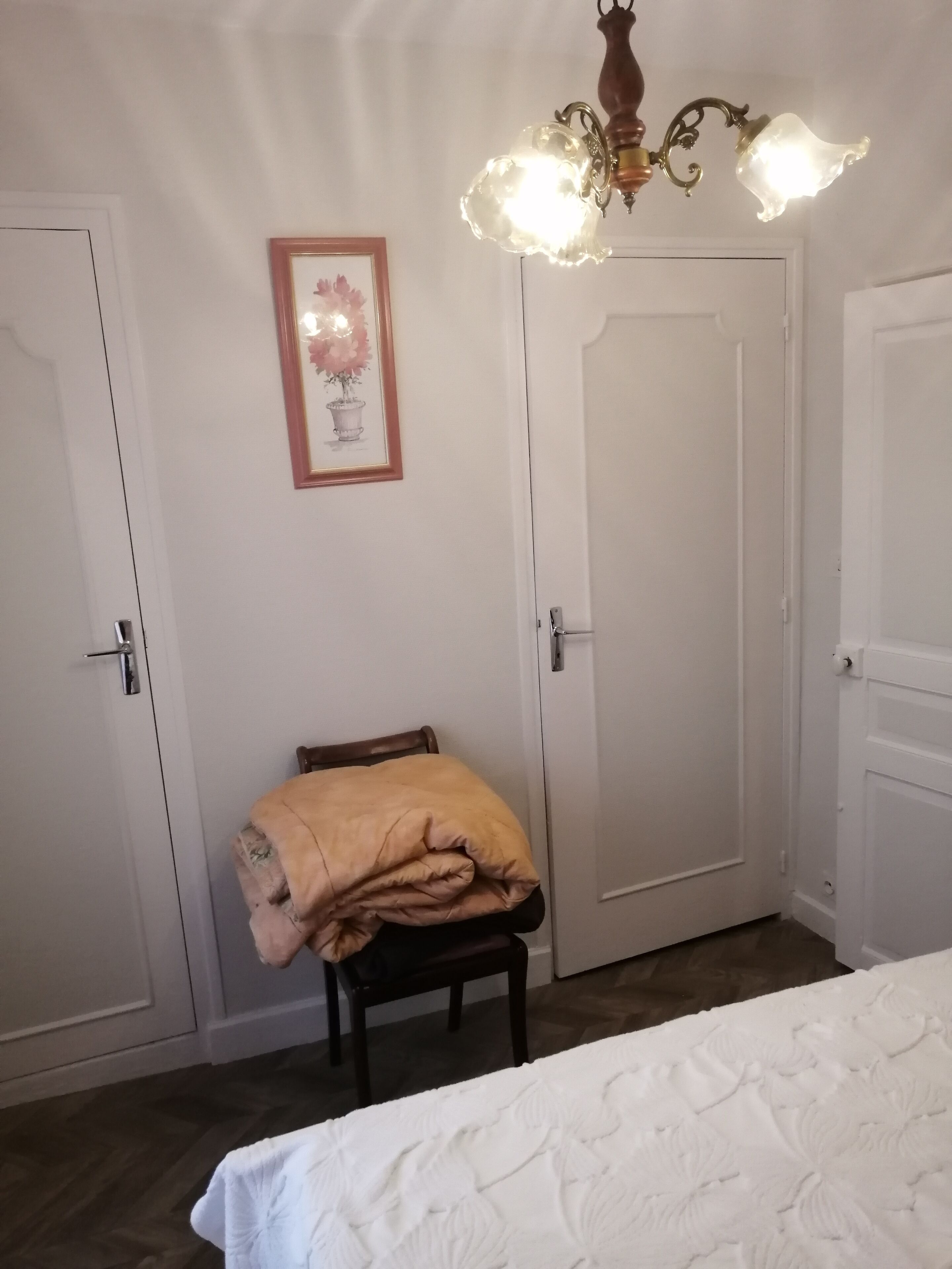 Ein Schlafzimmer mit einem Bett, einem Sessel mit Decke, einer Tür und einer Wandleuchte.