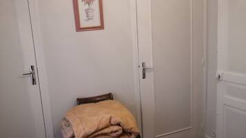 Ein Schlafzimmer mit einem Bett, einem Sessel mit Decke, einer Tür und einer Wandleuchte.
