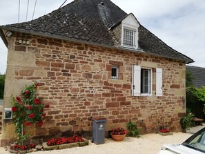 A stone building with a tiled roof, a small window with white shutters, and a flower box with red flowers. - Country house 10m from Brive and Aubazine (Lanteuil)