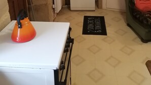 Una cocina compacta con un refrigerador blanco, una tetera y una silla verde.