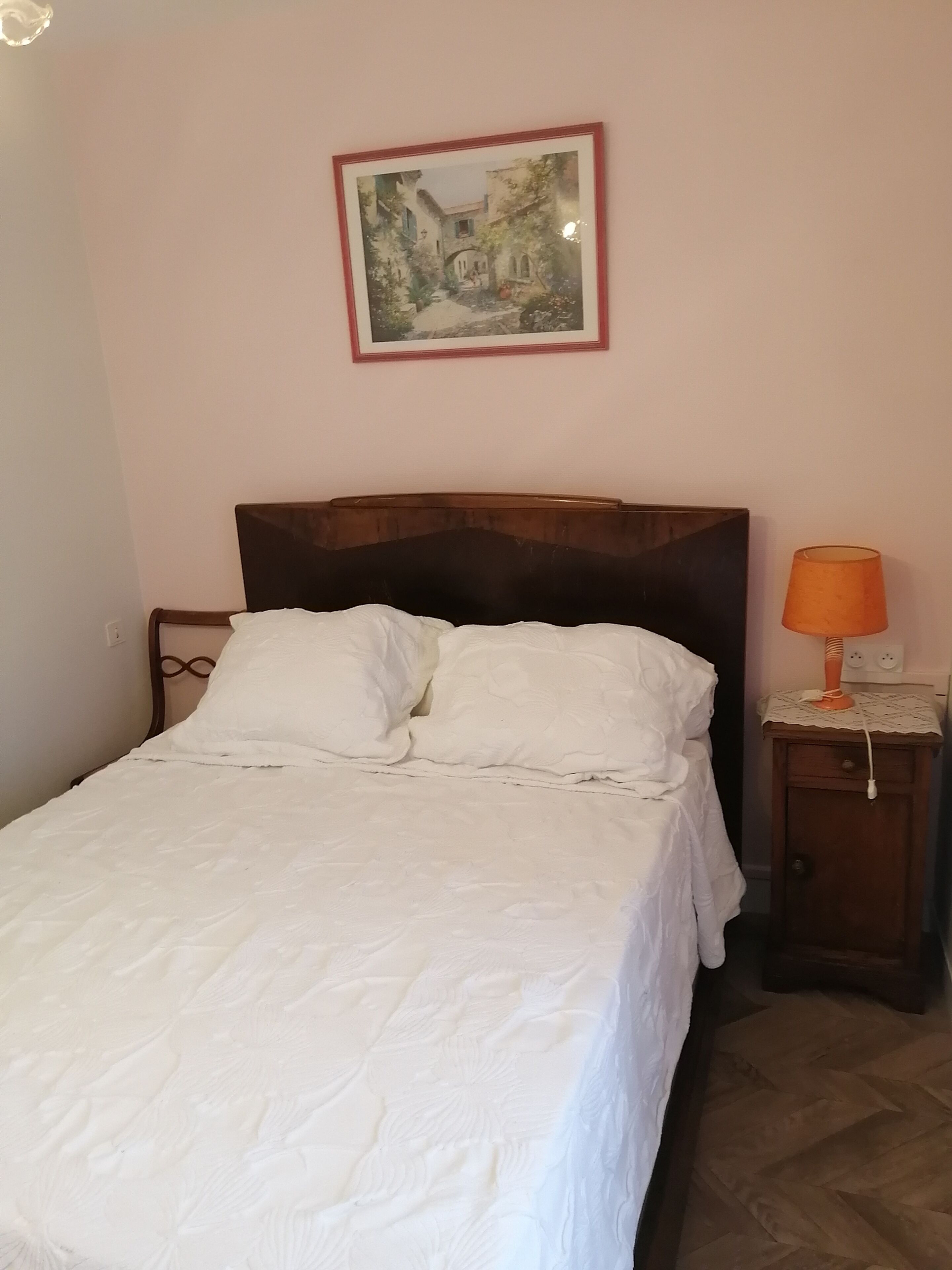 Een net opgemaakt bed met witte lakens in een kamer met een houten hoofdeinde.