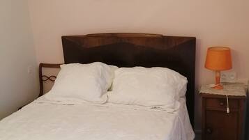 Een net opgemaakt bed met witte lakens in een kamer met een houten hoofdeinde.