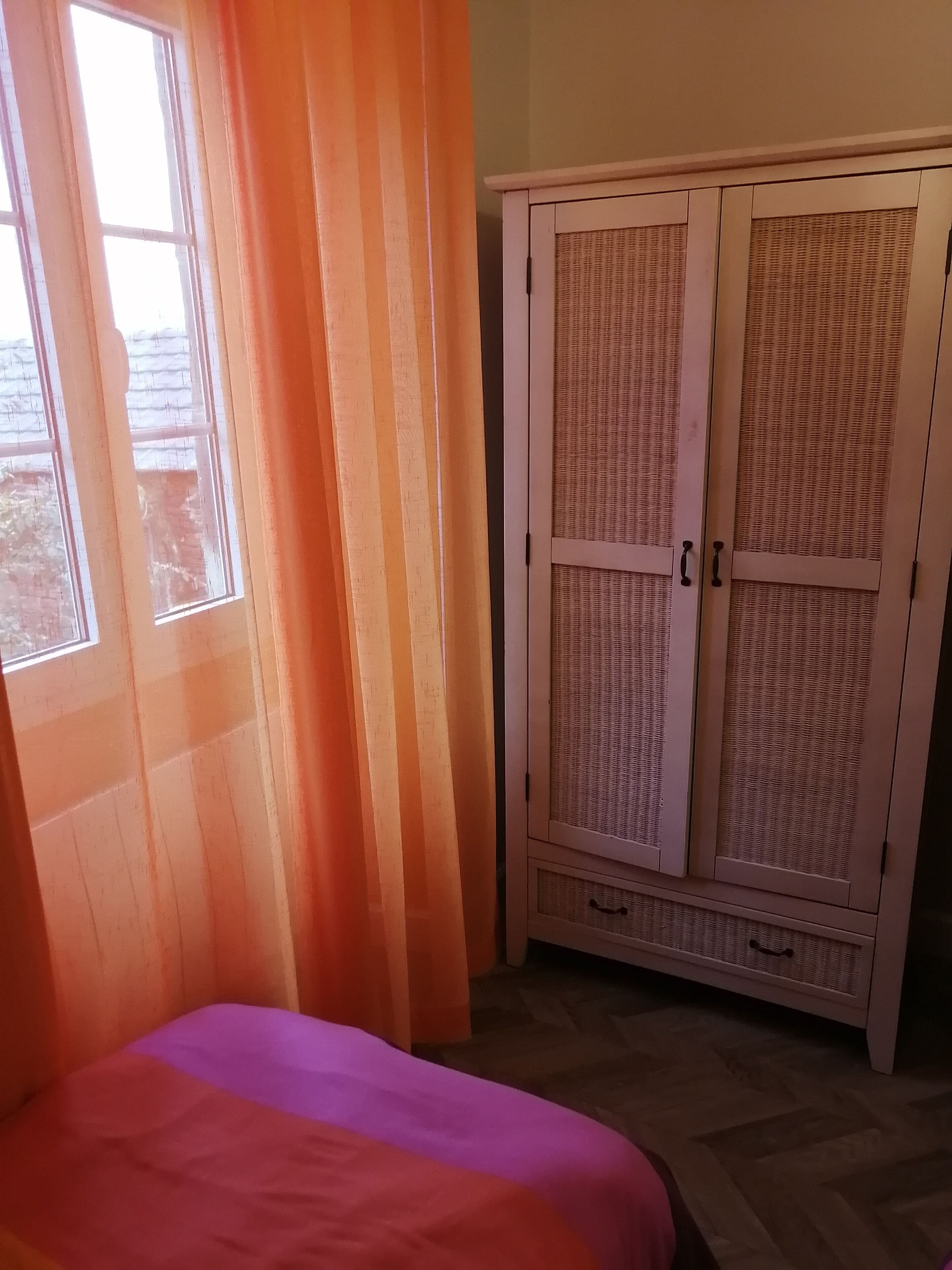 Una habitación con cama, armario y ventana con cortinas.