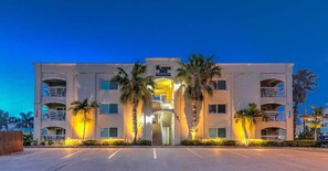 A multi-story hotel with a central entrance, balconies, and palm trees.