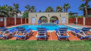 Una piscina con sillones de descanso, un área techada con puertas y palmeras.