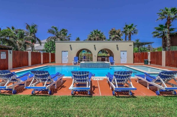A swimming pool with lounge chairs, a covered area with doors, and palm trees.