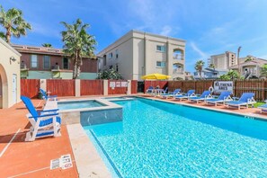 A swimming pool with lounge chairs, a wooden fence, and a building with balconies.