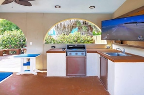 An outdoor kitchen with a gas stove, sink, and a TV mounted on the wall.