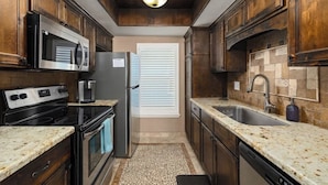 Cocina compacta con armarios de madera oscura, un refrigerador de acero inoxidable, un microondas, una estufa y un lavamanos.