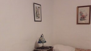 Une petite chambre à coucher avec deux lits, une table de chevet avec une lampe et deux tableaux encadrés accrochés aux murs.