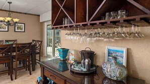 A dining area with a wooden table and chairs, a chandelier, and a wine rack with glasses.