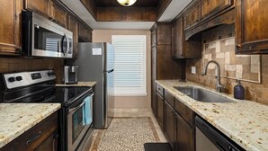 A compact kitchen with dark wood cabinets, a stainless steel refrigerator, a microwave, a stove, and a sink.