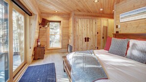A wooden cabin bedroom with a bed, a nightstand, a window, and a door. - Experience luxury in this 4-bedroom, 3.5-bath home in Breckenridge at Arrow Darrow! (Breckenridge)