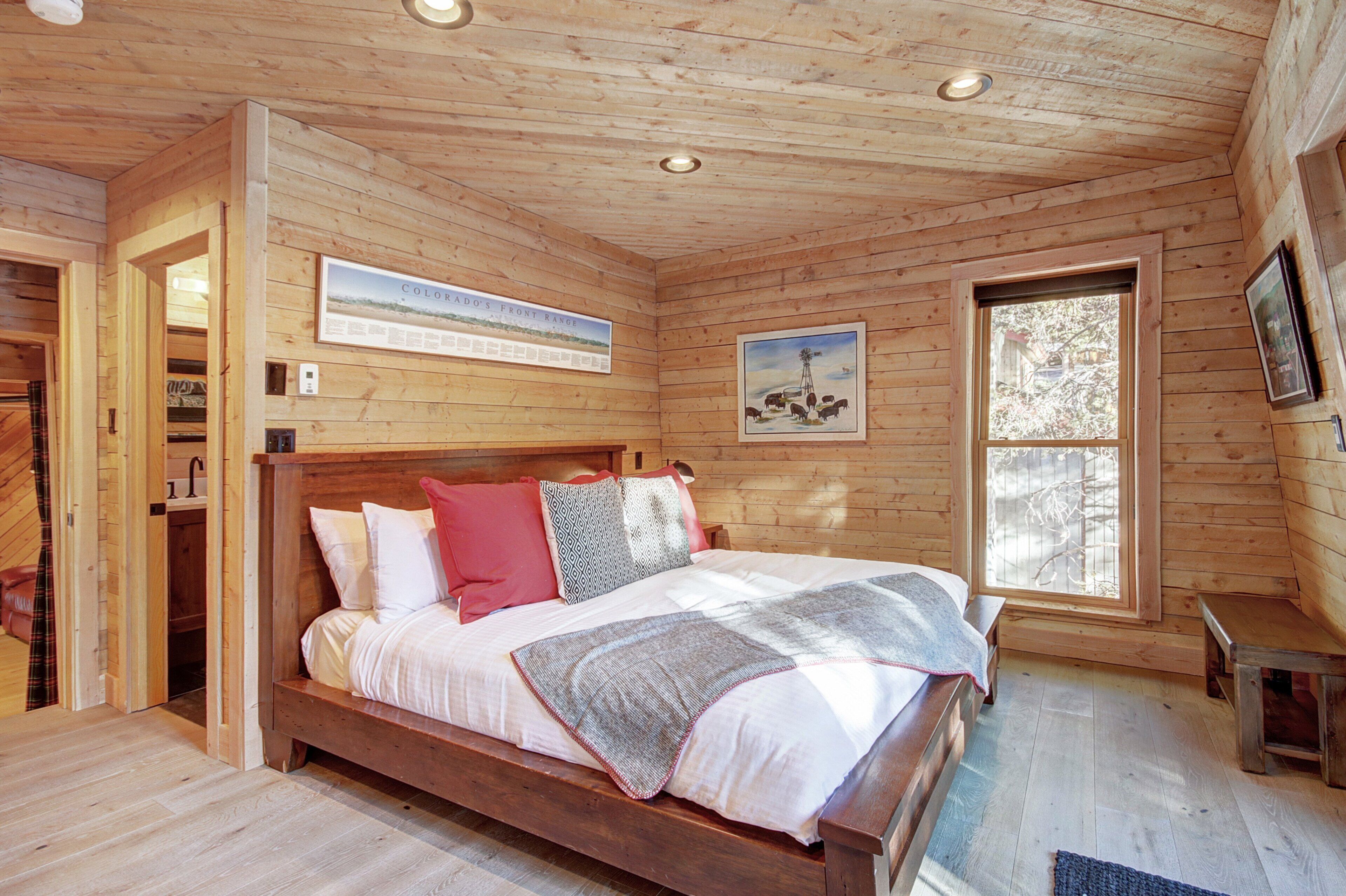 Une chambre dans une cabane en bois, avec un lit, une fenêtre et un tableau encadré au mur.