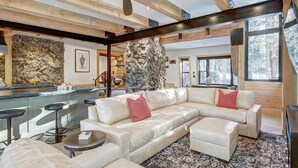 A spacious living area with a large sectional sofa, a stone accent wall, and a bar area with stools. - Experience luxury in this 4-bedroom, 3.5-bath home in Breckenridge at Arrow Darrow! (Breckenridge)