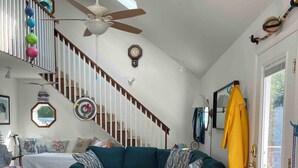 A spacious living room with a teal sofa, wooden dining table, and a staircase with a ceiling fan. - Saint Leonard Long Beach Beach House (St Leonard)