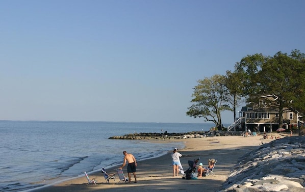 A beach with a house in the background, a rocky shoreline, and people near the water.
