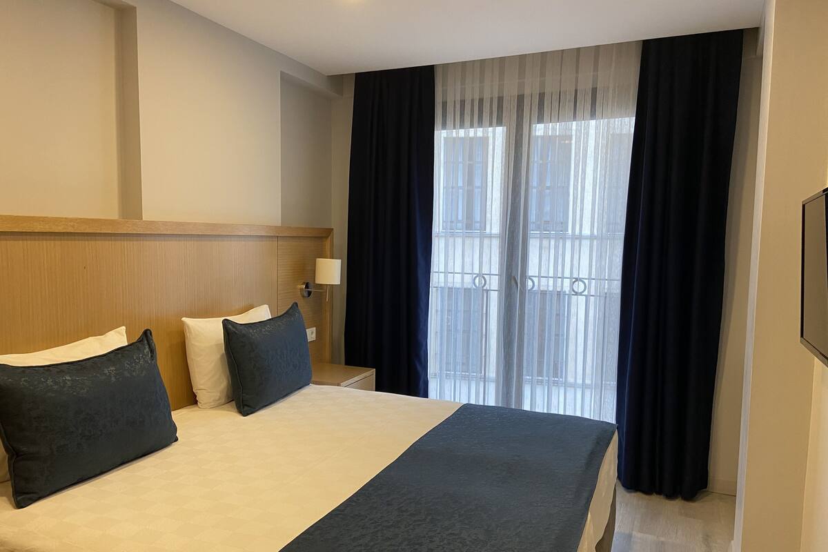A hotel room with a large bed, a nightstand, a lamp, and a window with curtains.