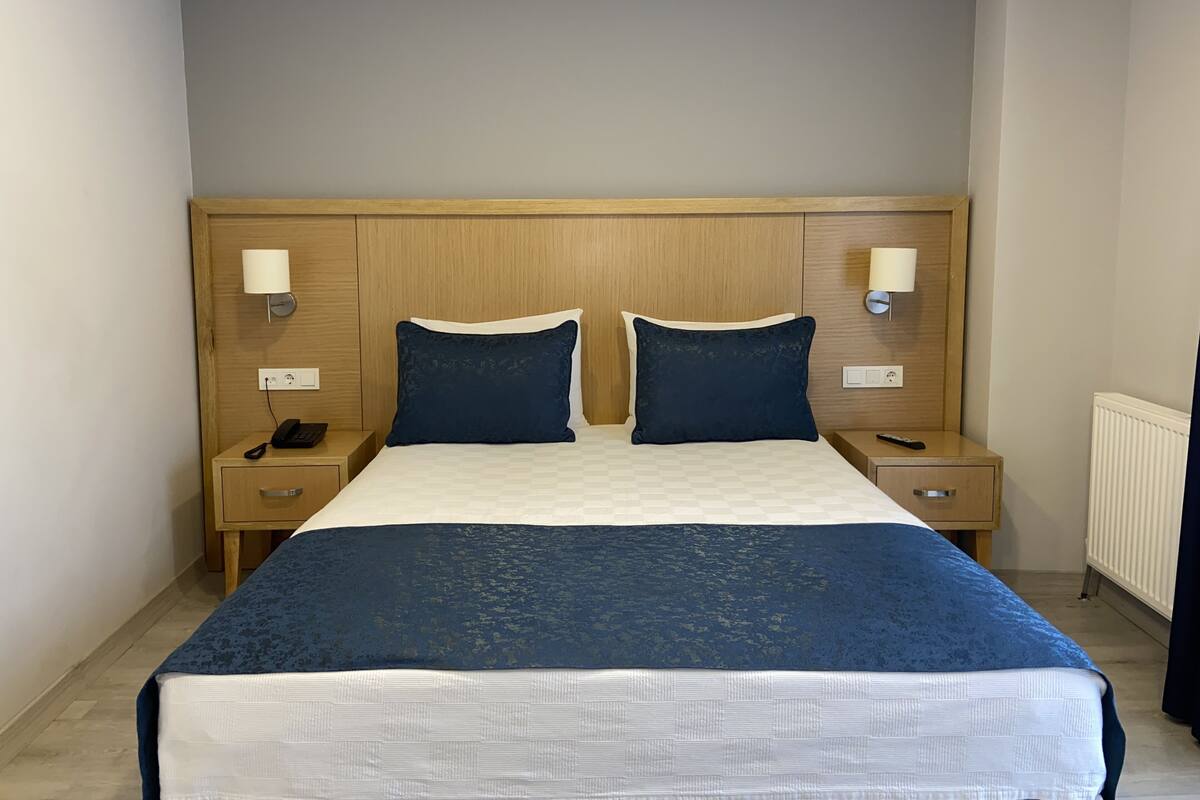A hotel room with a wooden headboard, two bedside lamps, a telephone, and a bed with a blue bedspread.