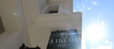 Un cartell d'hotel amb el nom "LIBERIA Hotel" sobre un mur blanc, amb una finestra i un llum penjada a la paret de fons.