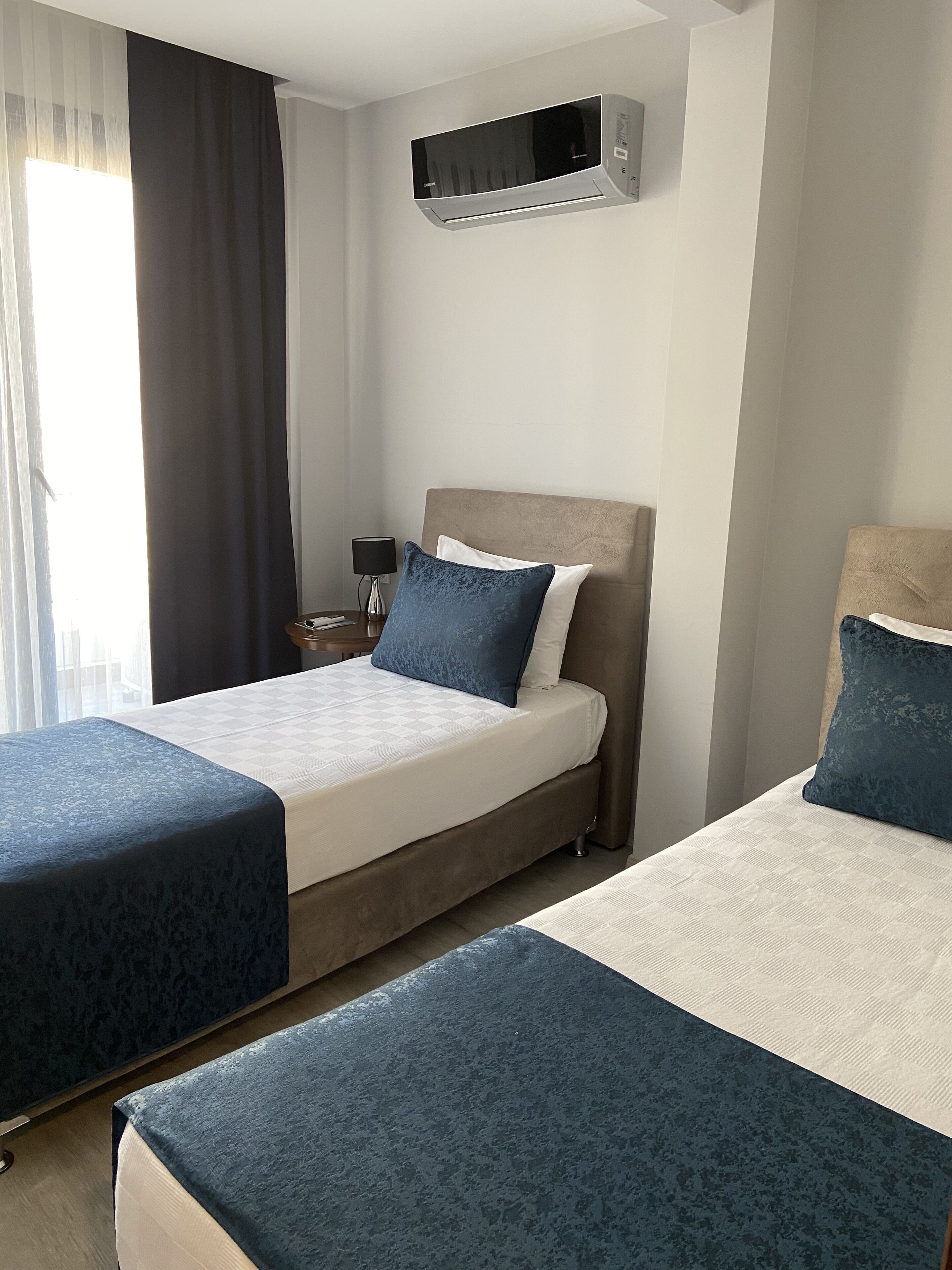 Habitación de hotel con dos camas, un televisor de pantalla plana, una lámpara y un ventanal con cortinas.