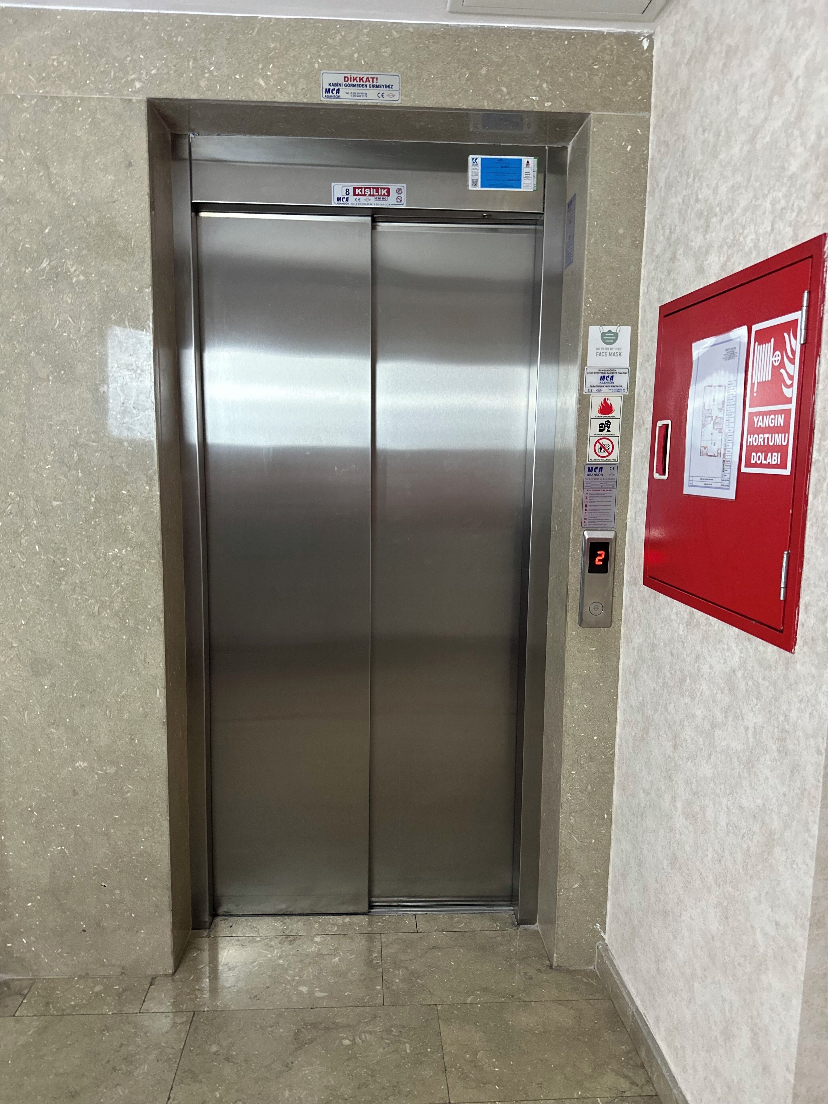 An elevator with a metallic finish, a digital display, and a fire safety sign on the wall.
