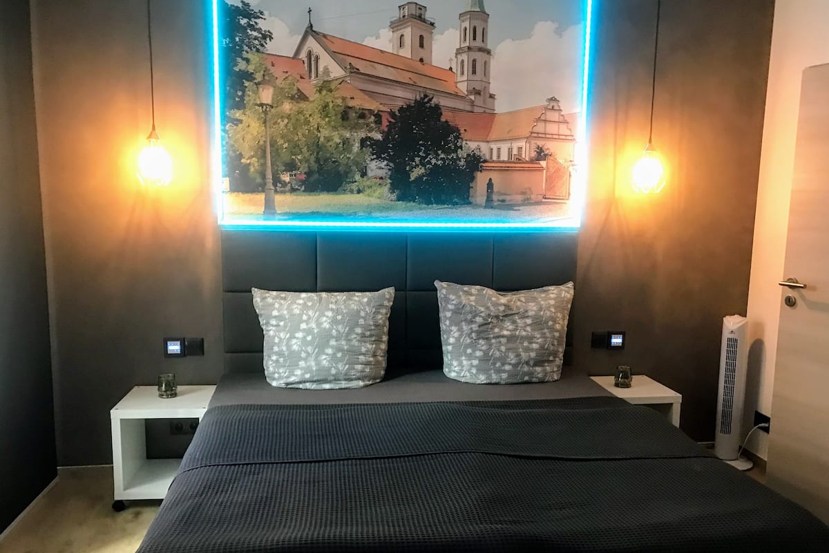 A modern bedroom with a large bed, two decorative pillows, a wall-mounted TV displaying a cityscape, and two bedside lamps.