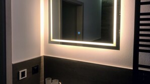 Un baño con un espejo grande, un perchero para toallas y un lavamanos pequeño.