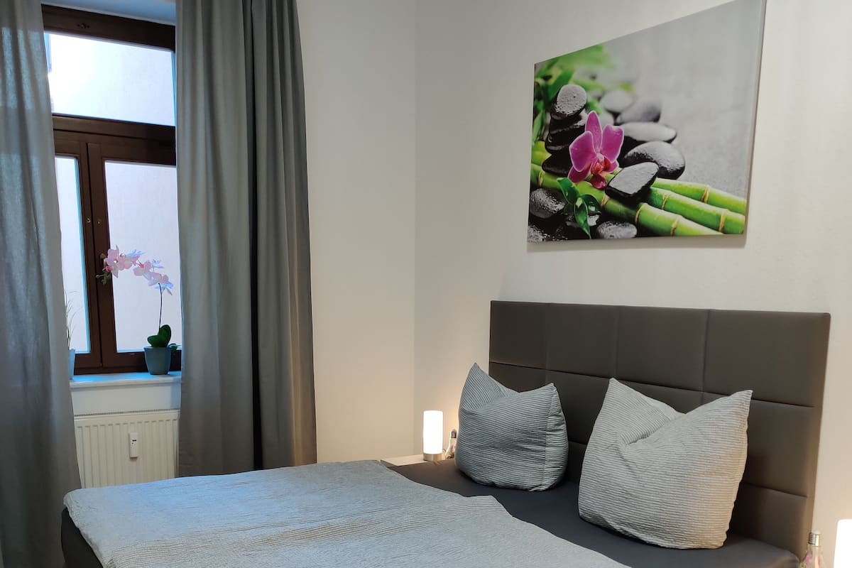 A bedroom with a bed, a nightstand, a window with curtains, and a wall-mounted picture.