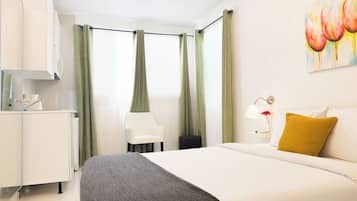 A hotel room with a bed, a desk, a chair, and a painting on the wall.