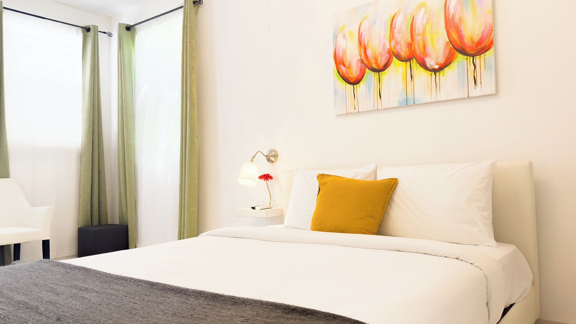 Une chambre d’hôtel avec un lit, une table de chevet avec une lampe, un tableau au mur et une fenêtre avec des rideaux.