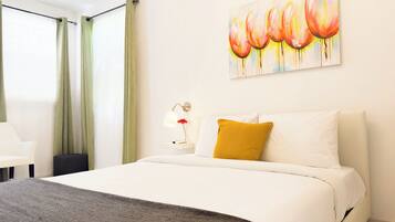 Una habitación de hotel con cama, mesita de noche con lámpara, un cuadro en la pared y ventana con cortinas.