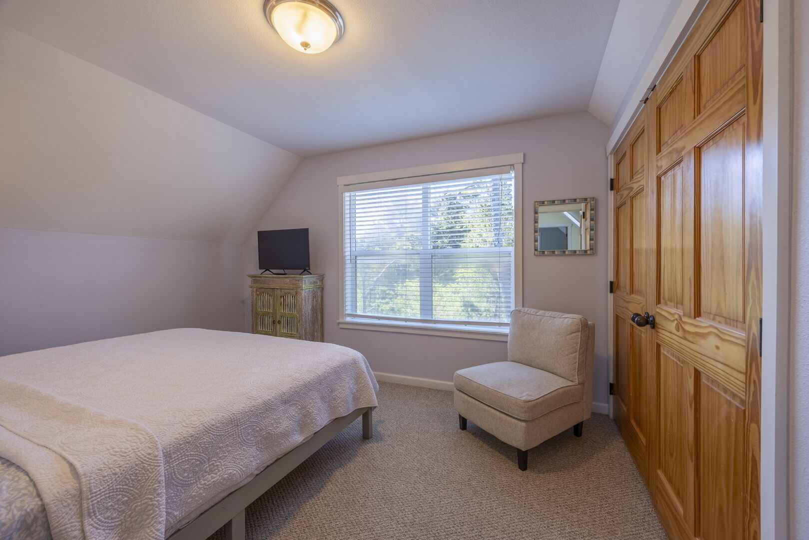 A bedroom with a bed, a chair, a TV, a window, and a wardrobe.