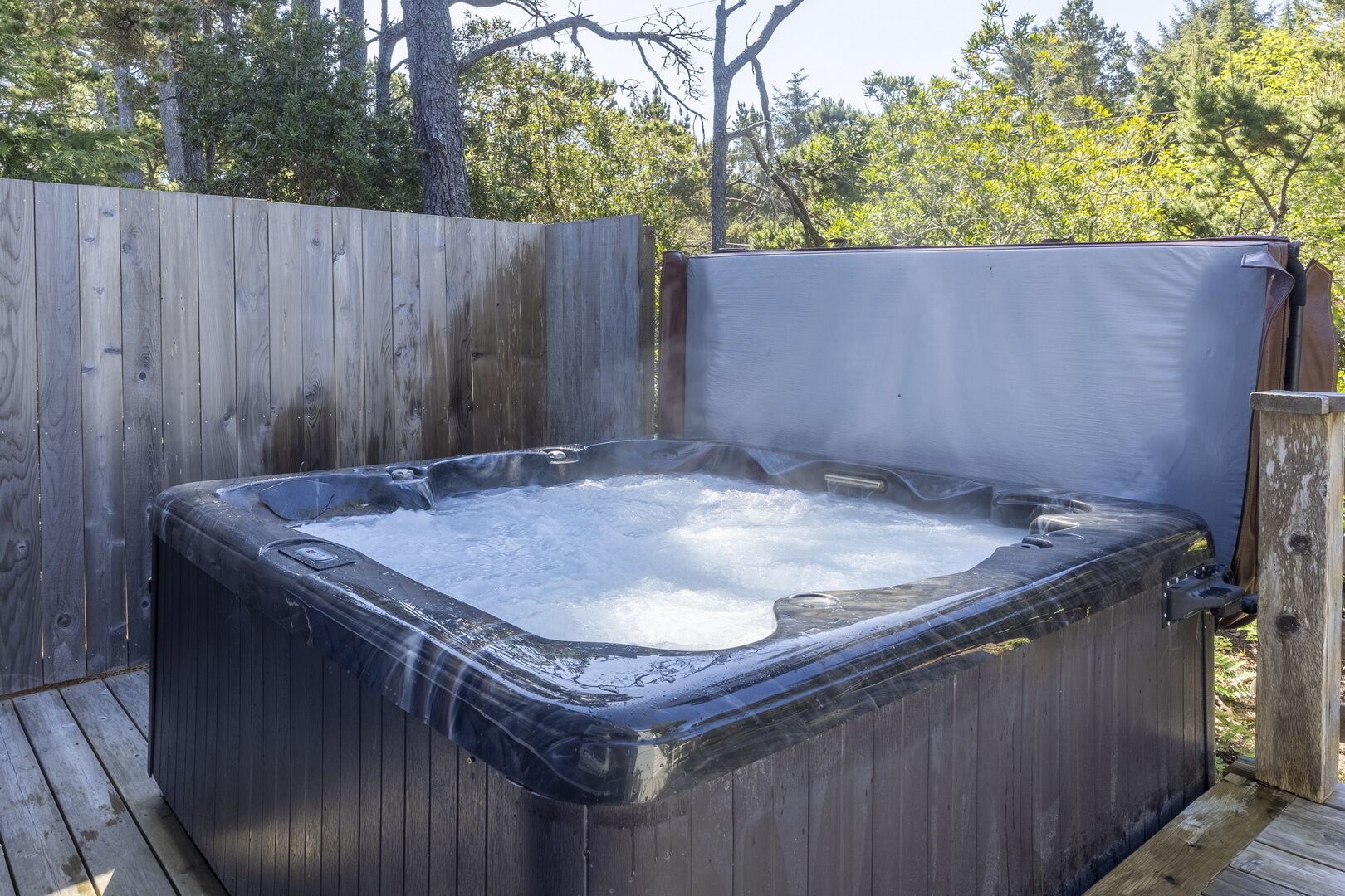 Un jacuzzi en un entorno exterior con una terraza de madera y una valla de madera al fondo.