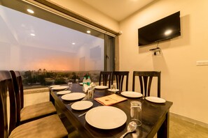 A dining table set with plates, cutlery, and glasses, with a view of a cityscape through a large window.