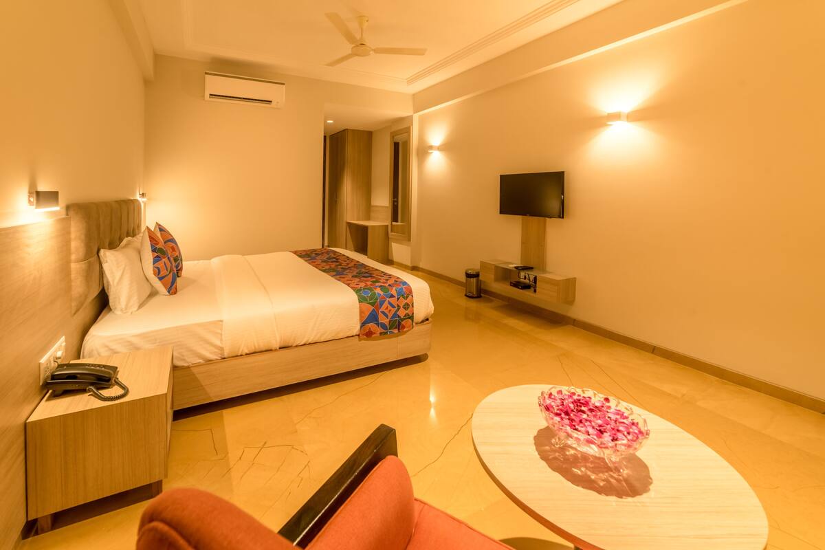 Habitación de hotel con cama, mesita de noche, silla, televisor y una mesa con un arreglo floral.
