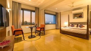 Habitación de hotel con cama con dosel, una mesa de comedor con sillas, una pequeña mesa redonda y vista a la ciudad al anochecer.