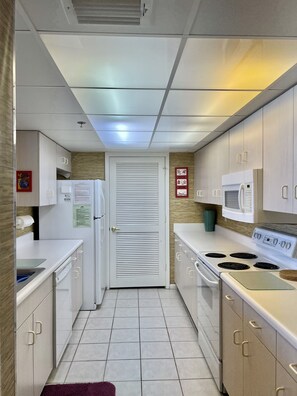 A modern kitchen with white cabinets, a stove, a microwave, and a refrigerator. - Flexible Policies: Affordable #4 *Beach Front* Condo  Amazing View!!!  (Panama City Beach)