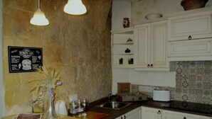 A kitchen with white cabinets, a tiled backsplash, a hanging light fixture, and a menu board on the wall. - Tal-Kapilluna Zebbug Guest House (Zebbug)