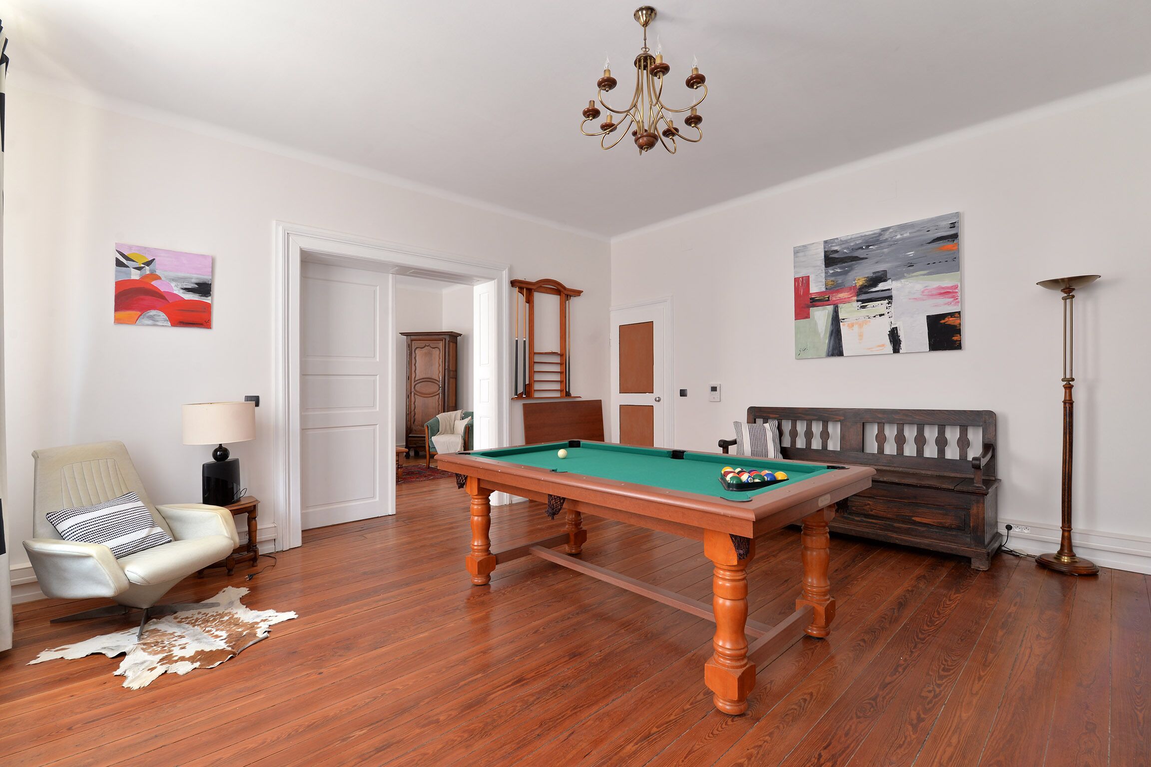 Una habitación con mesa de billar, sofá, sillón, lámpara y obras de arte en las paredes.