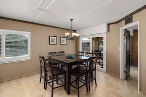 A dining area with a table and chairs, a chandelier, and a window with blinds.