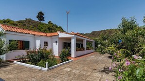 A white building with a red-tiled roof, surrounded by a garden with various plants and flowers. - GC0152 Holiday cottage in La Lechuza (Vega de San Mateo)