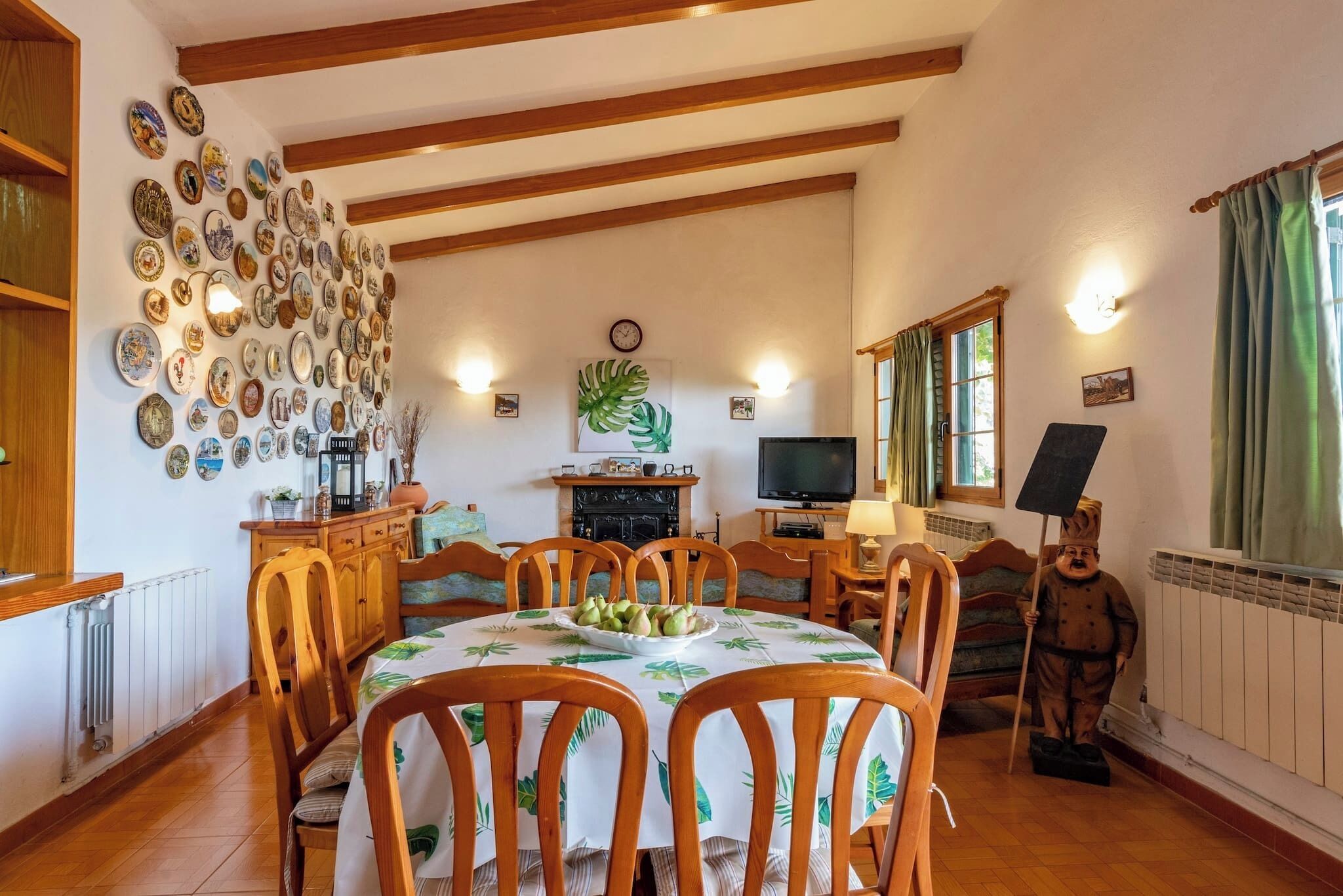 Un coin repas avec une table et des chaises en bois, une cheminée, un téléviseur et une statue.