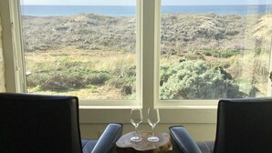 Ein Zimmer mit zwei schwarzen Stühlen und einem kleinen Holztisch mit zwei Weingläsern, mit Blick auf eine Küstenlandschaft.