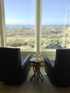 A room with two black chairs and a small wooden table with two wine glasses, overlooking a coastal landscape.