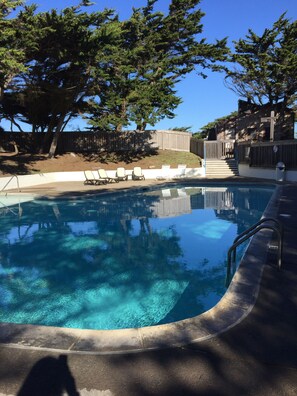 A swimming pool with clear water, surrounded by lounge chairs and a wooden fence.