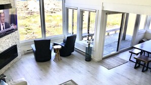 Ein großzügiger Wohnbereich mit einem großen Fenster mit Blick auf einen Strand, ausgestattet mit einer Couch, Sesseln und einem kleinen Tisch.