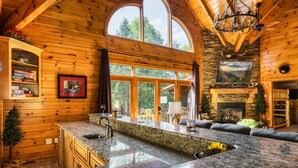 Una cocina amplia con encimeras de granito, chimenea de piedra y grandes ventanales con vistas al exterior.